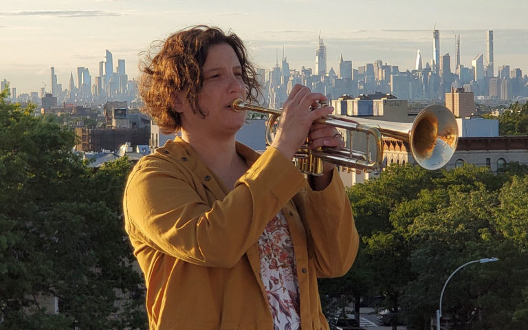 Samantha Boashnack playing a trumpet with the Seattle cityscape in the background.